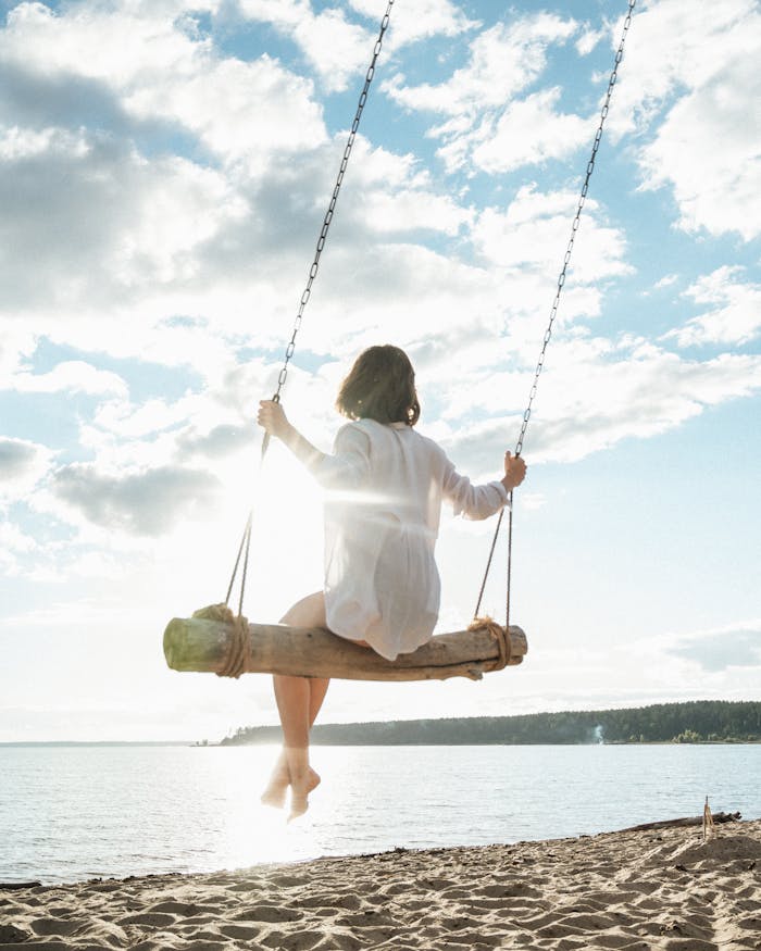 pexels-photo-8663572 Woman enjoys a peaceful moment on a beach swing with a beautiful ocean view at sunset.